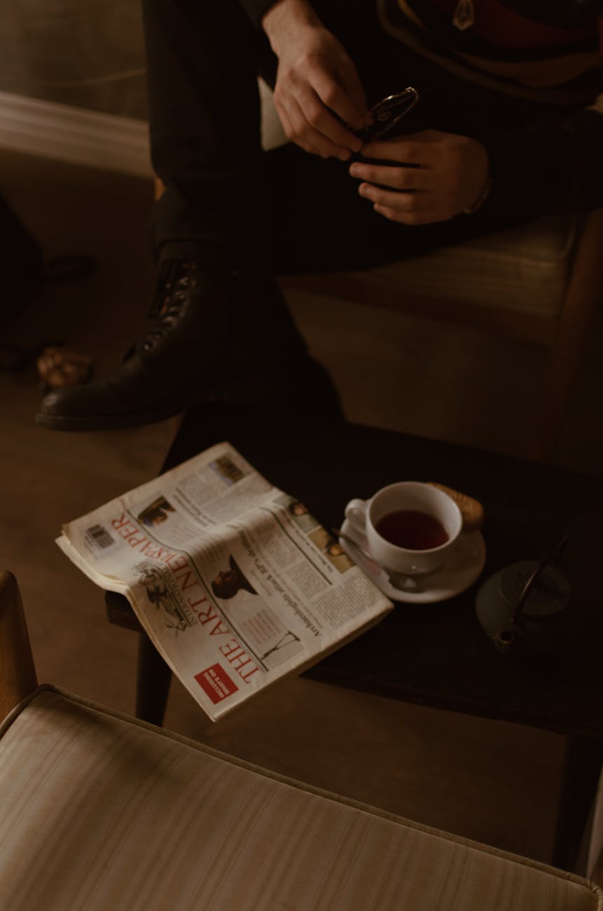 crop male reading newspaper in cafe during teatime