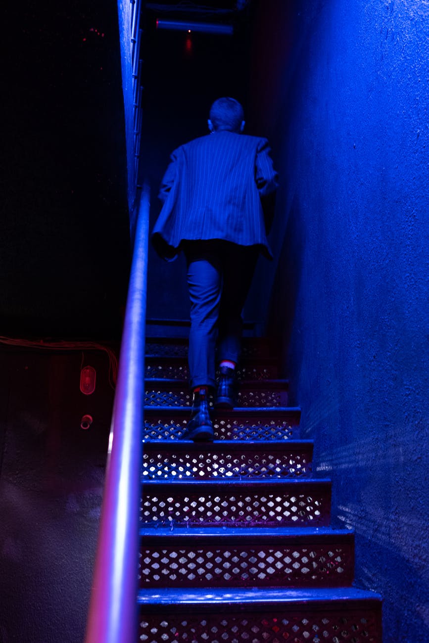 man in blue and white plaid dress shirt and black pants standing on staircase